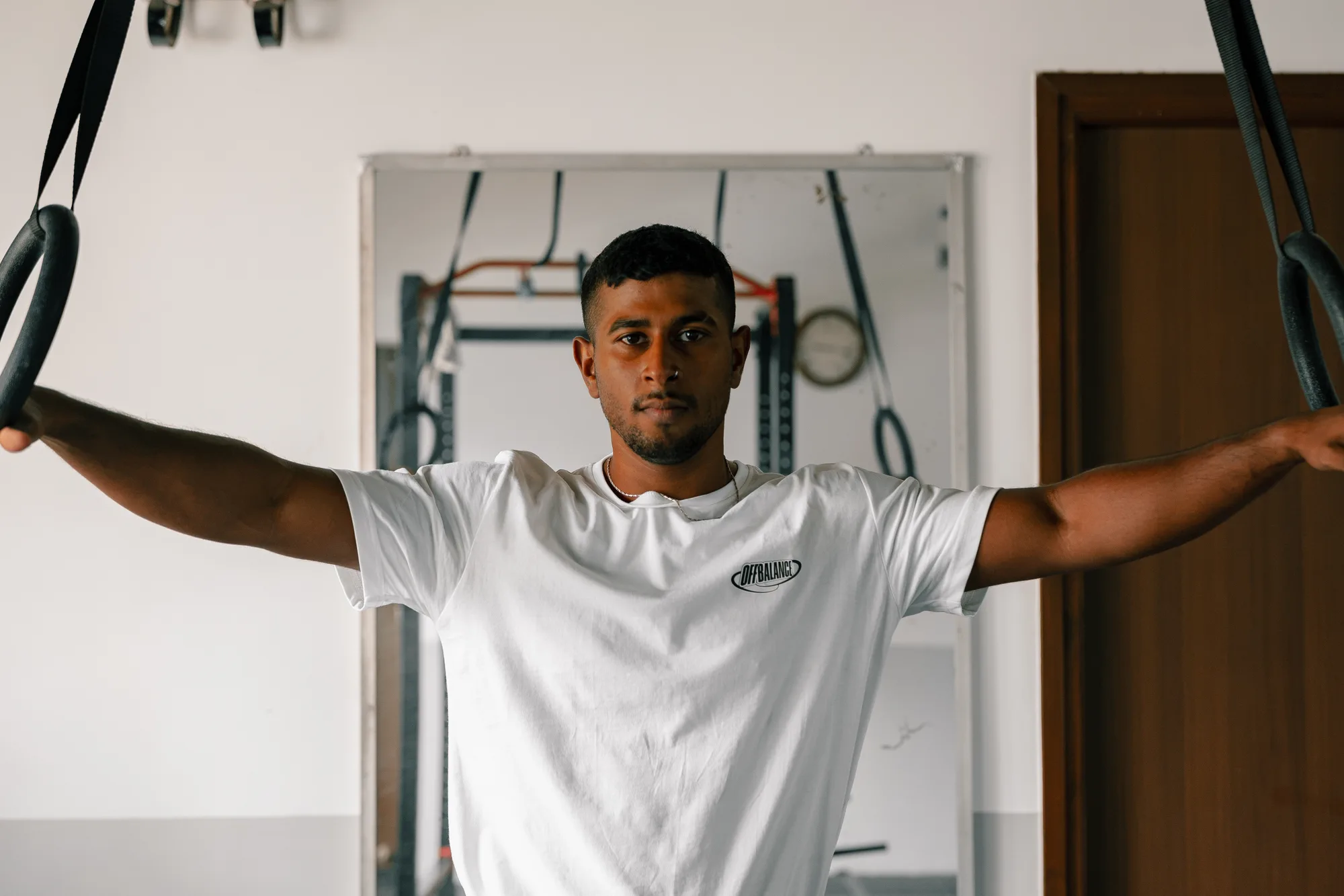 CJ holding gymnastic rings and looking at the camera in an Off Balance shirt