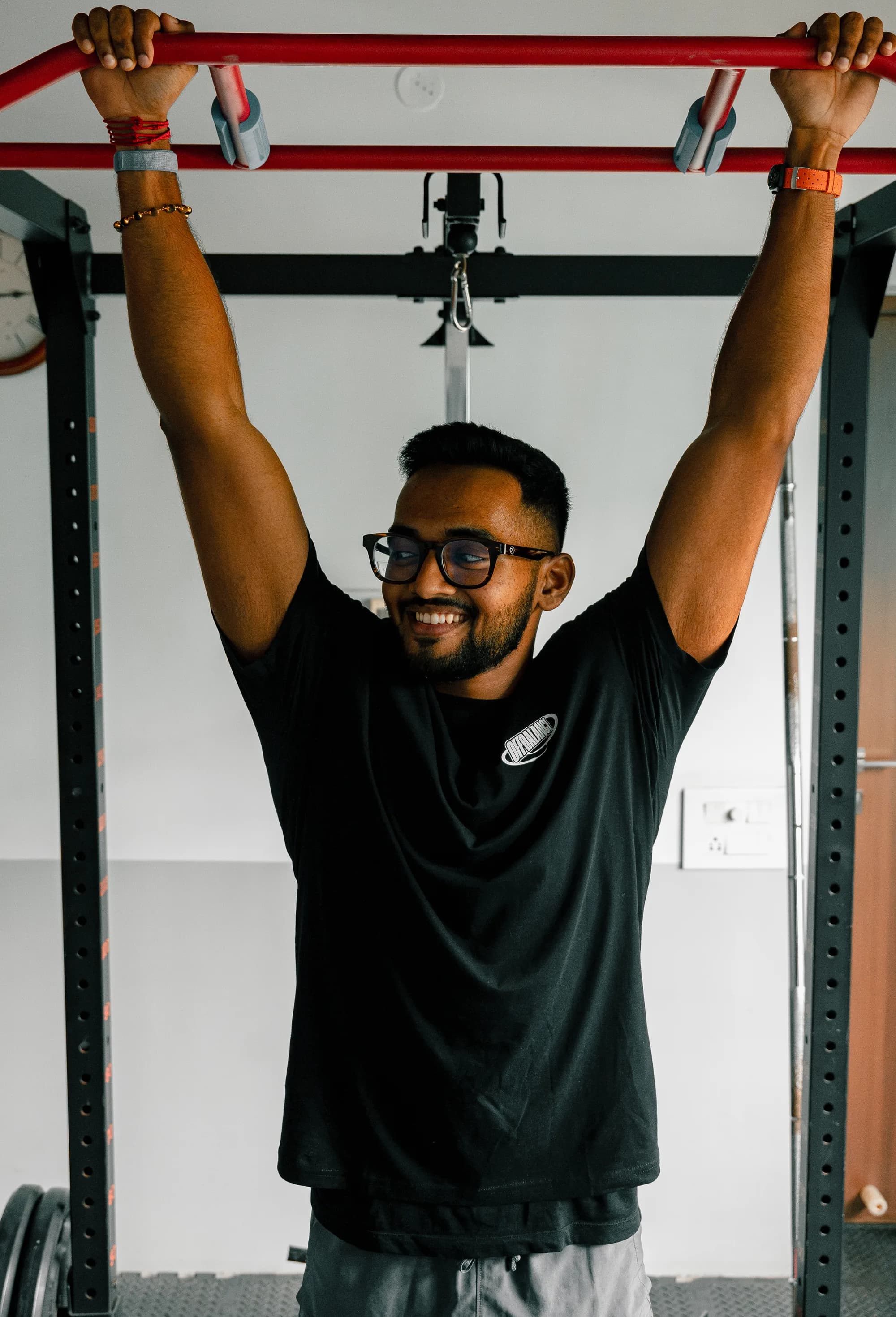 Achuthan hanging from a pull-up bar and smiling in the Off Balance training space